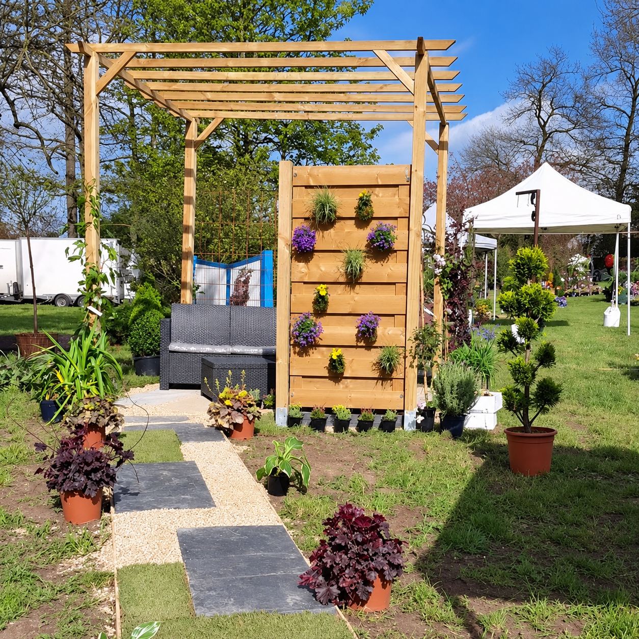 Un jardin aménagé avec une pergola en bois, un mur végétal en lattes de bois fleuri, un salon de jardin et une allée en dalles et gravier.