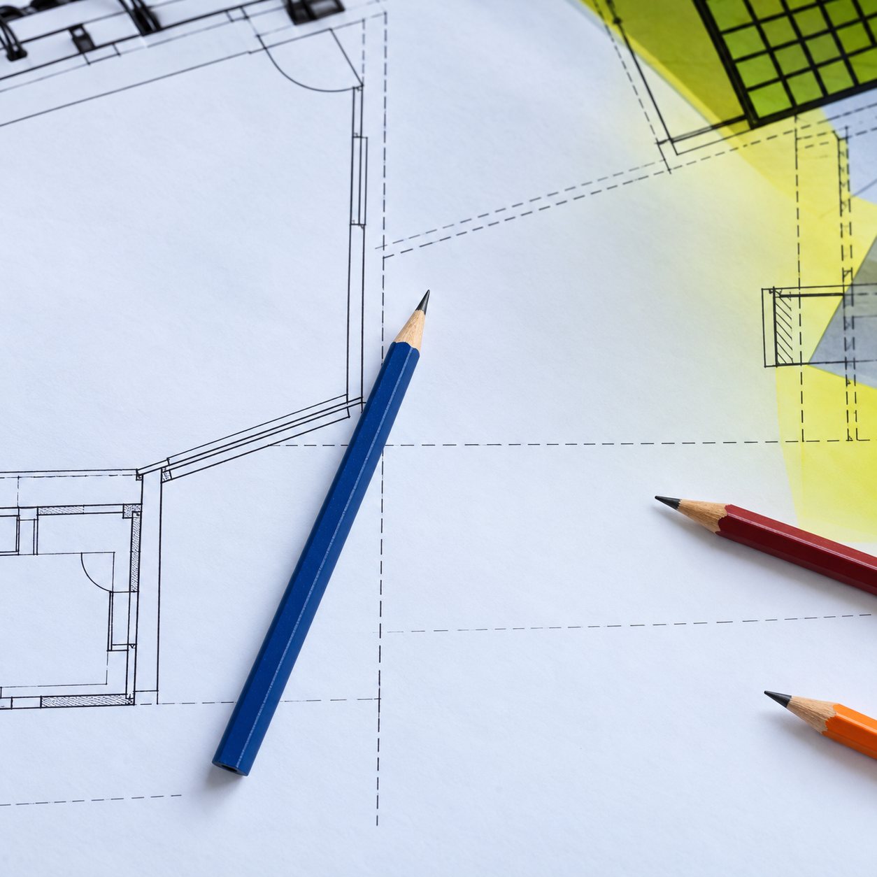 Des plans de construction dessinés sont étalés sur une table, avec un crayon bleu et des crayons de couleur posés dessus.